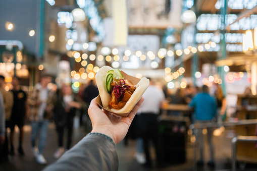 Personal perspective shot of a woman's hand holding a bao bun with tofu at a street market