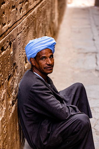 Local Egyptian man sitting in front of ancient Egyptian relics at the Temple of Horus in Edfu, Egypt.