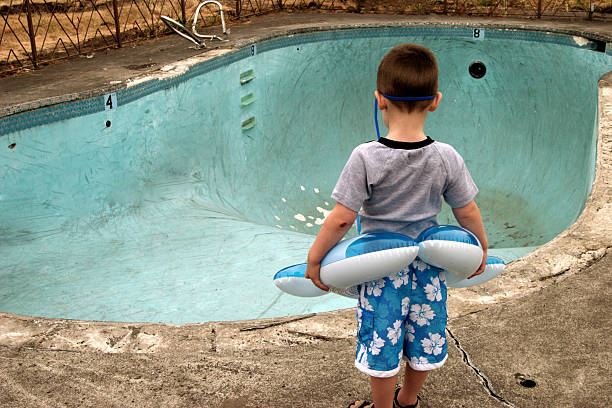 Small Boy Looking at Empty Pool Small boy wearing a floaty and goggles stares at an empty swimming pool. broken toy stock pictures, royalty-free photos & images