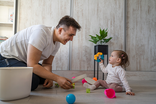 baby girl and her father young caucasian man with daughter playing at home happy sitting on the floor with toys in day fatherhood childhood family concept real people copy space