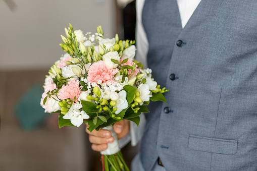 Hand of groom in wedding suit holding soft bridal bouquet of fresh flowers closeup. Elegant attribute of bride image and wonderful tradition. Beautiful and romantic wedding, luxurious celebration.
