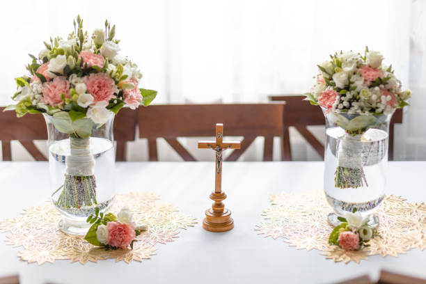 weiche brautsträuße frischer blumen in glasvasen und kirchenkreuz auf dem festtisch im restaurant. elegantes attribut und tradition. schöne und romantische hochzeit, luxuriöse feier - cluster verlobungsringe stock-fotos und bilder