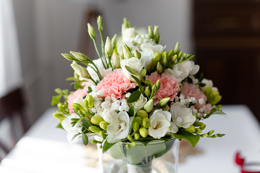Soft bridal bouquet of fresh flowers in glass vase on celebratory table closeup, blurred background. Elegant attribute and tradition. Beautiful and romantic wedding, luxurious celebration.