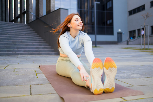 Woman training outdoors. She`s sitting on mat and doing yoga exercises