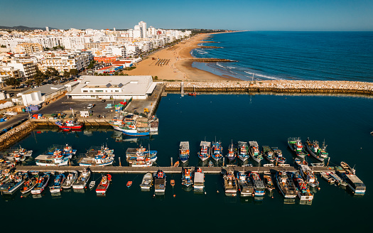 Beautiful aerial cityscapes of the tourist Portuguese city of Quarteira. Fishing boats on dock on foreground and tourists sunbathing in the background on a summer afternoon