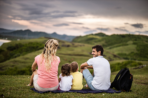 Rear view of happy family communicating while relaxing on a hill. Copy space.