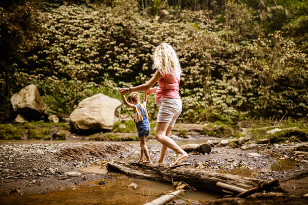 istock Single pregnant mother assisting her daughter in walking over tree trunk. 1399638007