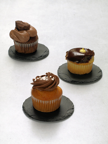 Chocolate cupcakes are served on black slate plates and isolated on a grey background.