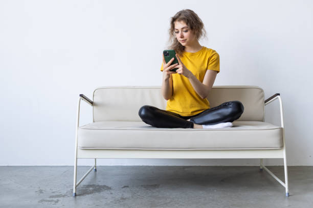 istock Happy young woman using mobile phone while sitting a couch at home with laptop computer 1399640723