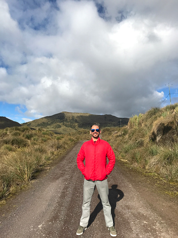 Young handsome latin male backpacker hiking and enjoying his vacation time walking and hiking on the Sierra's Highlands, in front of Pichincha, Cayambe, Cotopaxi's Volcanoes with a blue sky in a midday near to Quito, Pichincha's Province, Ecuador, Latin America.