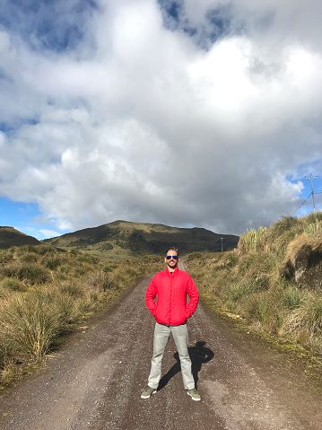 Young handsome latin male backpacker hiking and enjoying his vacation time walking and hiking on the Sierra's Highlands, in front of Pichincha, Cayambe, Cotopaxi's Volcanoes with a blue sky in a midday near to Quito, Pichincha's Province, Ecuador, Latin America.