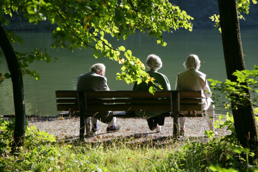 Three seniors enjoying the silence on a park bench with view to a lake.