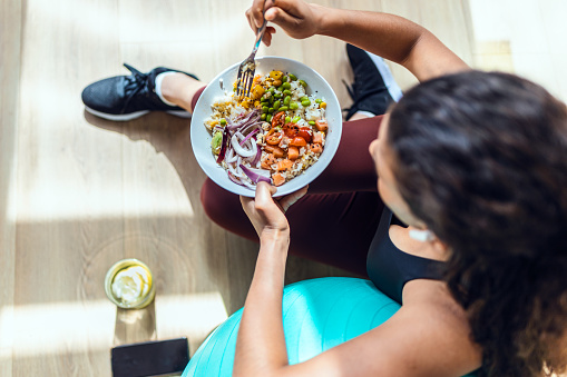 Shot of sporty young woman eating healthy while listening to music sitting on the floor at home.