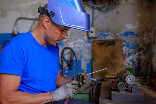 Trabajador metalúrgico con guantes de soldadura y mascarilla preparándose para trabajar con una máquina de soldar en un taller familiar. Mano de obra calificada. photo