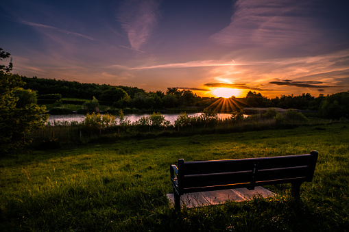 Dramatic and calming sunset over lake in English countryside watched over by empty park bench