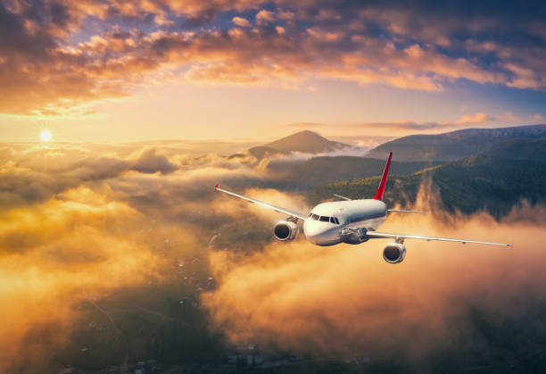 飛行機は夏の日没時に雲の上を飛んでいます。旅客機、山々、オレンジ色の空がある風景。航空機が離陸中です。出張中です。民間航空機。航空写真。輸送 - airplane taking off sky commercial airplane ストックフォトと画像