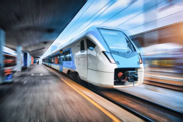 High speed train in motion on the railway station at sunset. Blue modern intercity passenger train with motion blur effect on the railway platform. Railroad in Europe. Commercial transportation