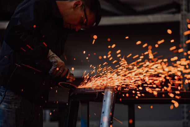 istock Heavy Industry Engineering Factory Interior with Industrial Worker Using Angle Grinder and Cutting a Metal Tube. Contractor in Safety Uniform and Hard Hat Manufacturing Metal Structures. 1399652538