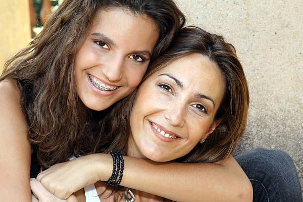 Portrait of smiling long haired mother and daughter posing outdoors. Brick wall is in the background.