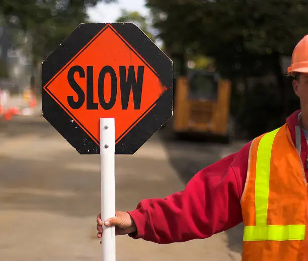 Flagger directing traffic, holding "Slow" sign