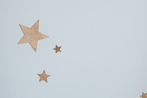 Close-up of decorative golden paper stars of different size on plain blue wall like sky.