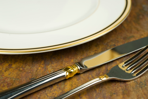 Closeup image of elegant silverware and plate on brown slate table.