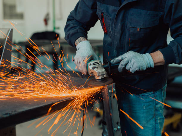 istock Heavy Industry Engineering Factory Interior with Industrial Worker Using Angle Grinder and Cutting a Metal Tube. Contractor in Safety Uniform and Hard Hat Manufacturing Metal Structures. 1399657753