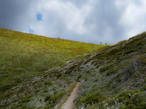 Distant hikers walking the Razorback at Mouth Hotham with stormy skies