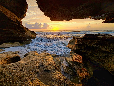View through a rock cavern of the sun rising over rushing water with clouds