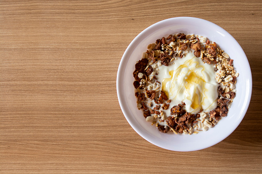 Granola, Yogurt, Honey, Cereal, and Banana on a White Plate on a wood background - Top View