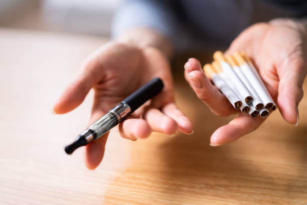 Woman Holding Vape And Tobacco Cigarettes Woman's Hand Holding Vape And Tobacco Cigarettes Over Wooden Desk electronic cigarette stock pictures, royalty-free photos & images