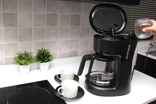 Woman's hands prepare delicious and aromatic coffee in coffee maker in the kitchen for breakfast