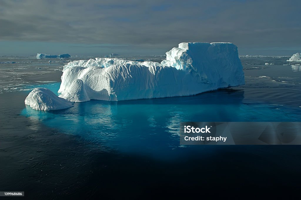 Antarctic iceberg with shimmering underwater ice A foot-shaped iceberg swimming in front of a marvellous antarctic iceberg scenery. The huge underwater part of the iceberg is shimmering through the water surface in bright blue colours. Iceberg - Ice Formation Stock Photo