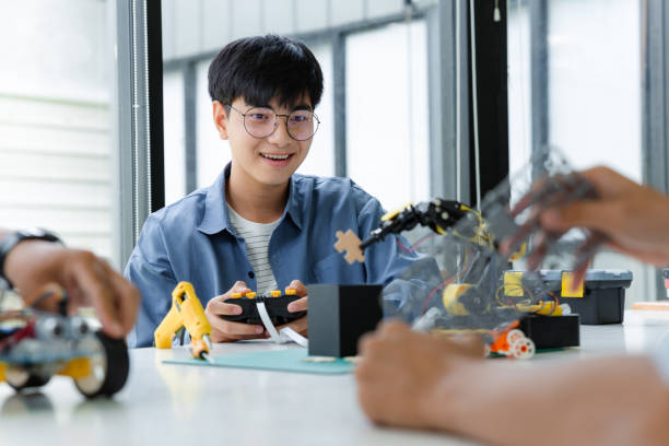 Asian teenager constructing robot arm project in science classroom. technology of robotics programing and STEM education concept.