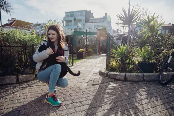 Photo of Young woman petting a stray black cat on a street