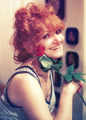 Grainy vintage portrait of a beautiful woman with a red rose and smiling at the camera.