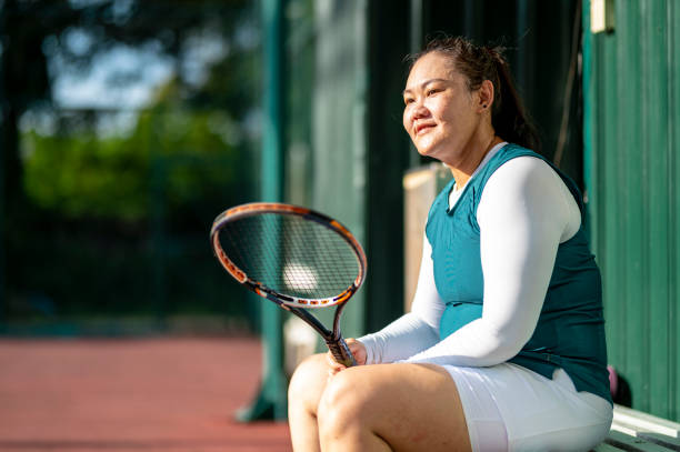 une femme adulte chinoise asiatique prend une pause et regarde un autre joueur de tennis sur un court de tennis - tennis women one person vitality photos et images de collection