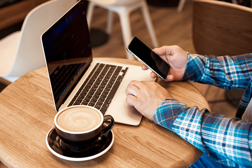 Hombre casual freelancer trabajando en línea con macbook y teléfono móvil y bebiendo café de la mañana en la cafetería photo