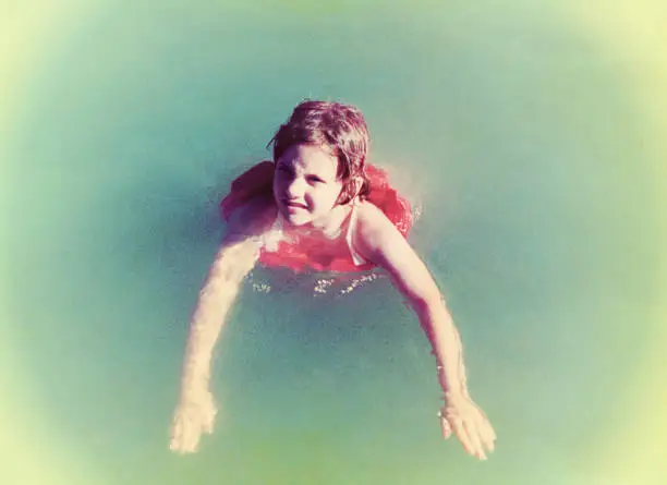 Vintage photo of a young girl swimming in a swimming pool with a life jacket on. Vintage photo from the seventies of the 20th century.