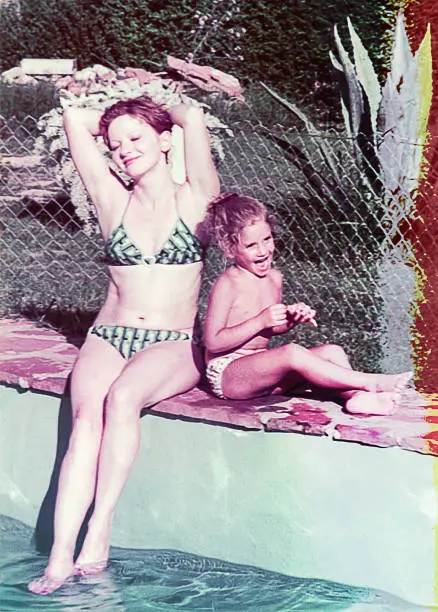 Vintage photo of mother and daughter, on a hot sunny day, at the edge of the swimming pool. Vintage image of a family summer vacation. Damaged vintage photo of the seventies of the 20th century.