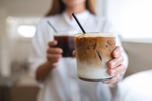 крупный план женщины, держащей и подающей два стакана кофе со льдом - latté стоковые фото и изображения