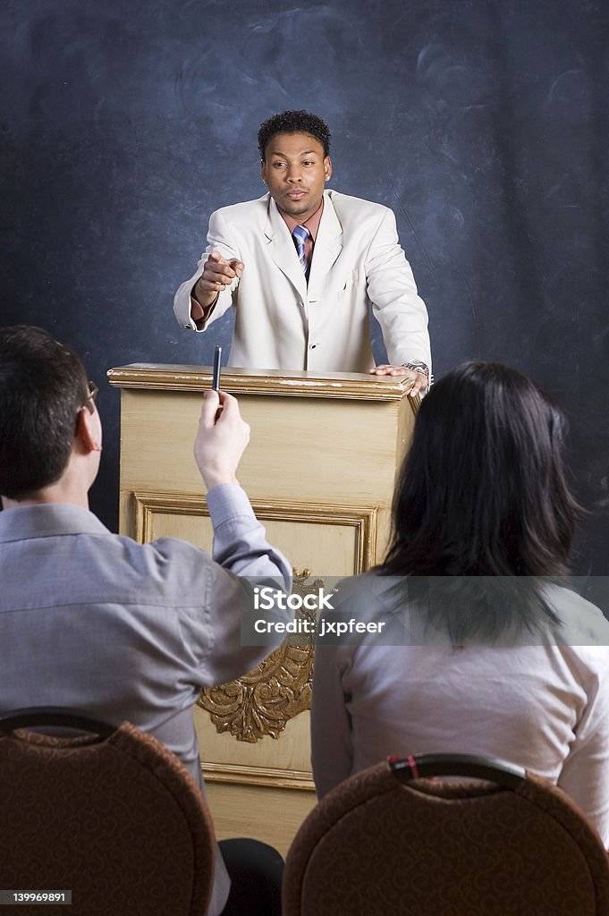 Answering a Question A man speaking from a podium, taking questions from his audience. Adult Stock Photo