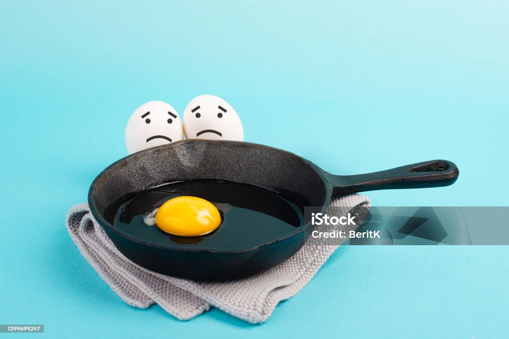 A fried egg in a pan, two friends look with sad faces at him, having a breakfast in the morning, funny food, broken friendship, healthy food Animal Egg Stock Photo