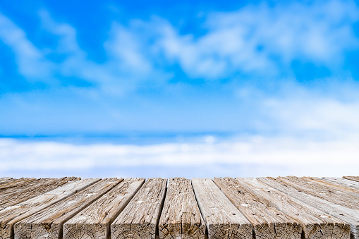 Summer abstract backgrounds. Empty rustic wooden table at the bottom of the frame with defocused blue sky and beach at background. Diminishing perspective on table. Focus on table. Copy space, ideal for product montage.