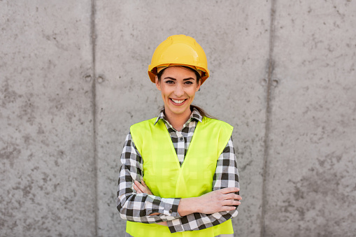 Portrait of a beautiful young female engineer at a construction site. Architect wearing safety helmet and protection gear.