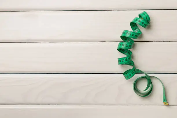 Green measuring tape on wooden background, top view.
