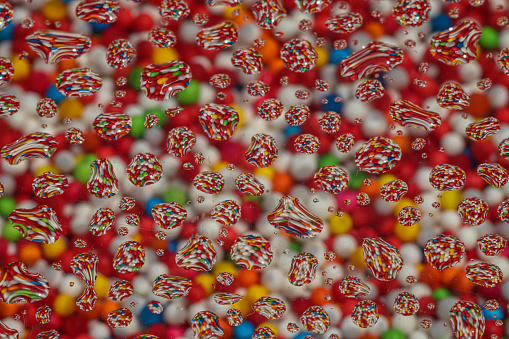 Multicolored sugar flakes and reflections of droplet water with bright sunlight for background.