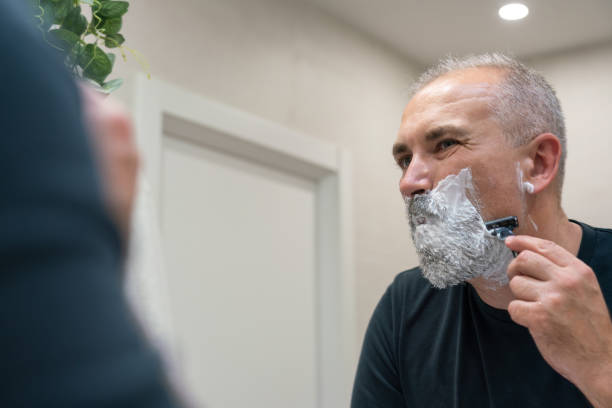 istock Middle aged handsom man trimming his beard and mustache standing in bathroom and looking in a mirror 1399705361
