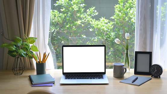 Front view laptop computer with blank screen, houseplant, picture frame and stationery on wooden table.