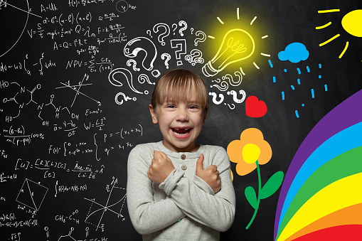 Funny young kid girl on blackboard background with science and arts pattern. Creativity education, new ideas and right and left hemispheres of the brain concept.